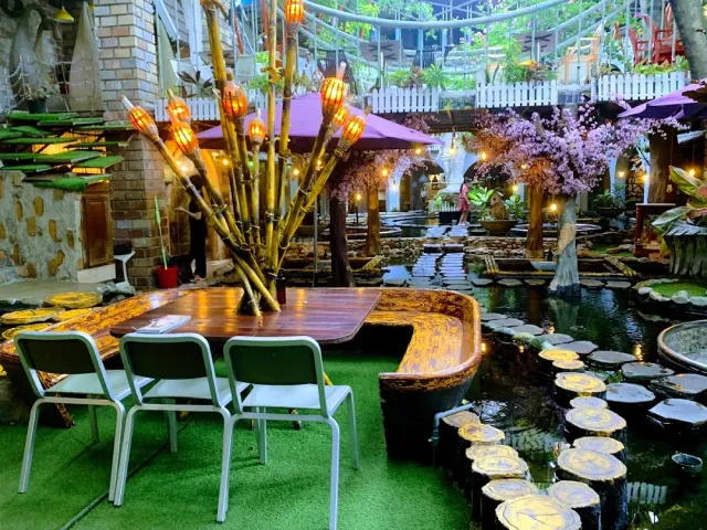 An artificial garden with a pond, wooden discs over the water, cane torches and purple parasols