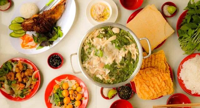 An overhead view of a steaming pot of greens, dishes on red plates and rice crackers