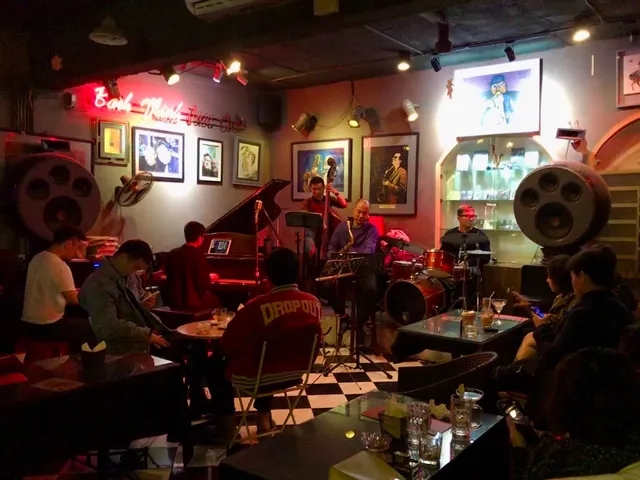 A jazz band plays in a corner with a grand piano and an audience at low tables