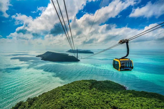 A cable car crossing turquoise water above a green island