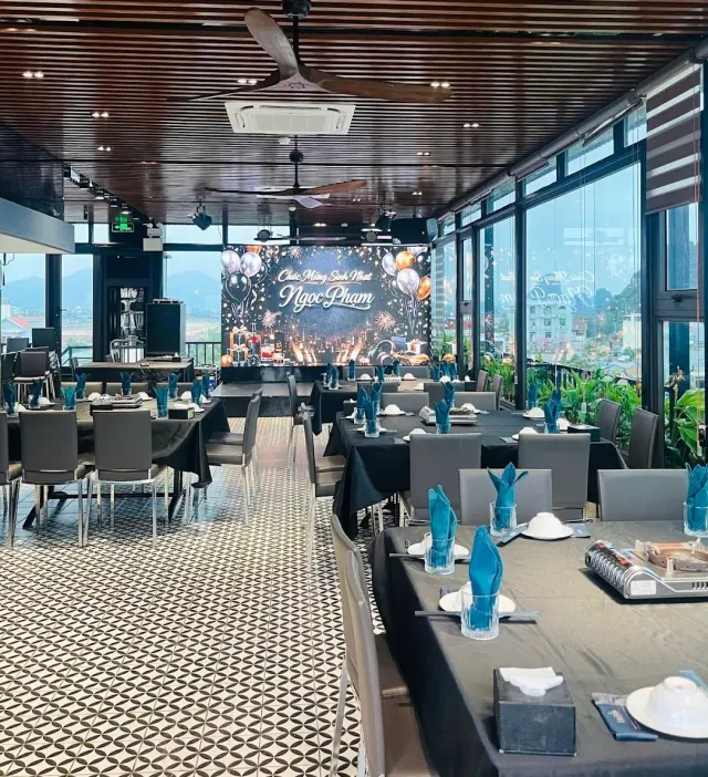A wide hall with tables in black cloths and blue napkins, panoramic windows and a decorated stage