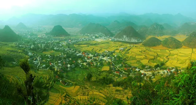 A panoramic view of a valley with conical hills, golden rice fields and village houses