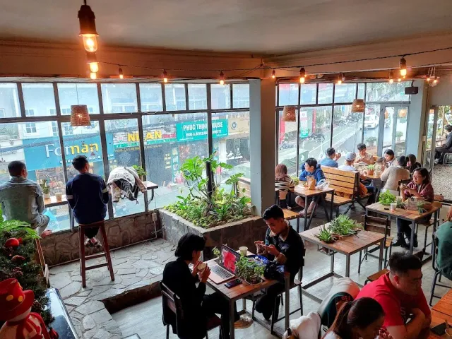 A space with large windows, hanging bulbs, planted beds and customers at wooden tables