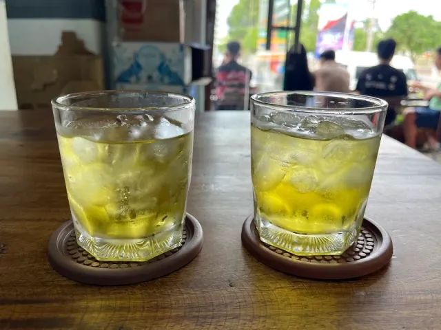 Two glasses of yellow iced drink on wooden coasters, with a blurred street behind