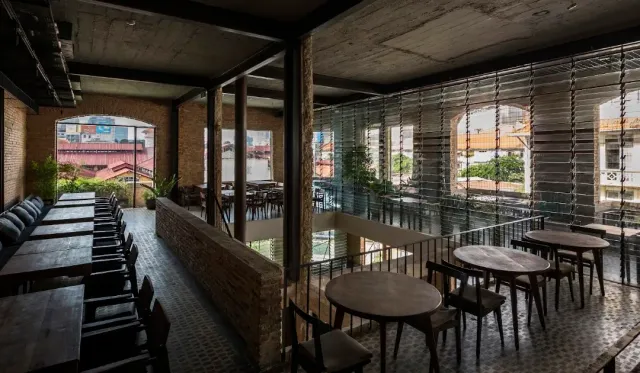 An industrial interior with a concrete ceiling, a brick wall, round wooden tables and a glass wall