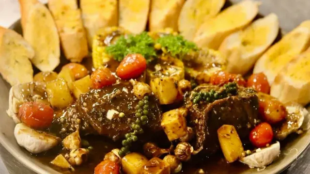 Beef chunks in sauce with cherry tomatoes, potatoes and green peppercorns, ringed with baguette slices