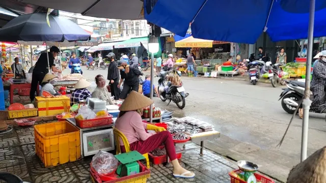 A street market under blue umbrellas, vendors in straw hats with trays of fish
