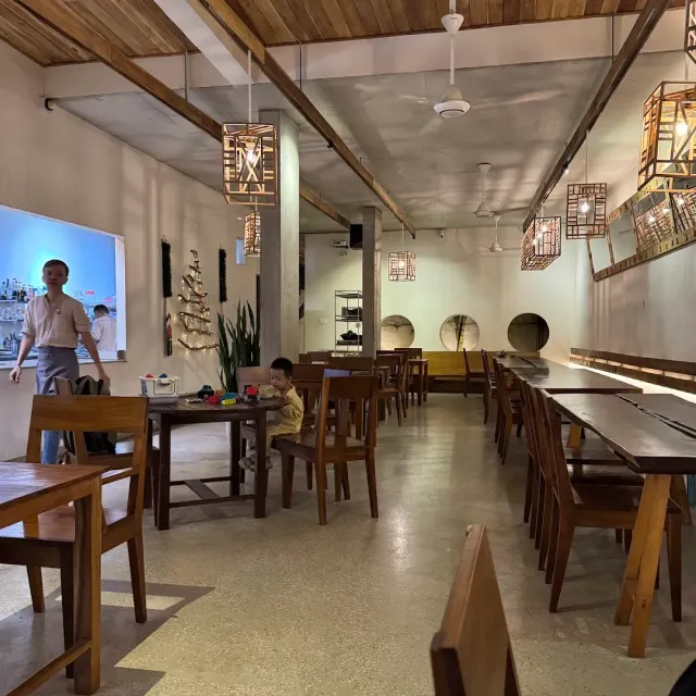 A long narrow hall with wooden tables, latticed hanging lamps and white walls