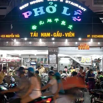 A colorful neon restaurant sign at night, motorbikes passing in a blur in front