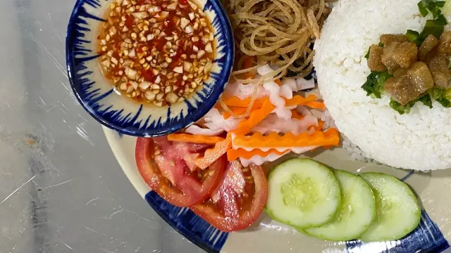 A plate with a mound of rice, tomato and cucumber slices and a small bowl of garlic chili sauce