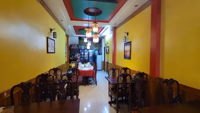 A narrow room with yellow walls, carved dark wooden chairs and a colorful recessed ceiling