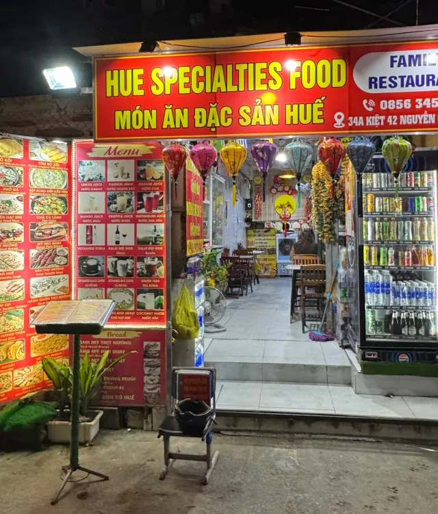 A storefront lit at night with a red sign, photographed menu boards and colorful silk lanterns