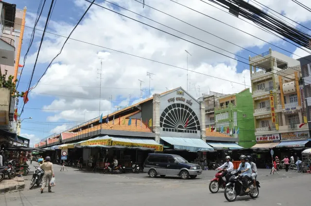 A street with a long building with an arched facade and yellow awnings, motorbikes and power lines