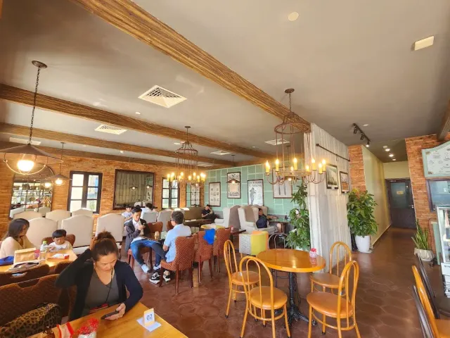 An interior with ceiling beams, iron chandeliers, brick walls and guests seated around tables