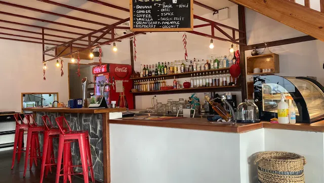 A bar counter with red stools, shelves of bottles and a chalkboard listing flavors