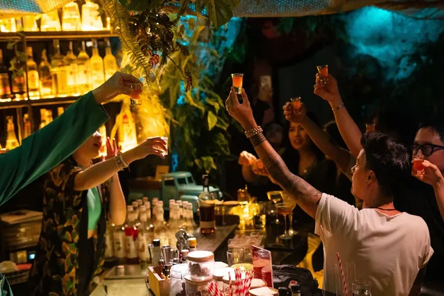 A group raises orange shot glasses in front of a bar counter surrounded by greenery