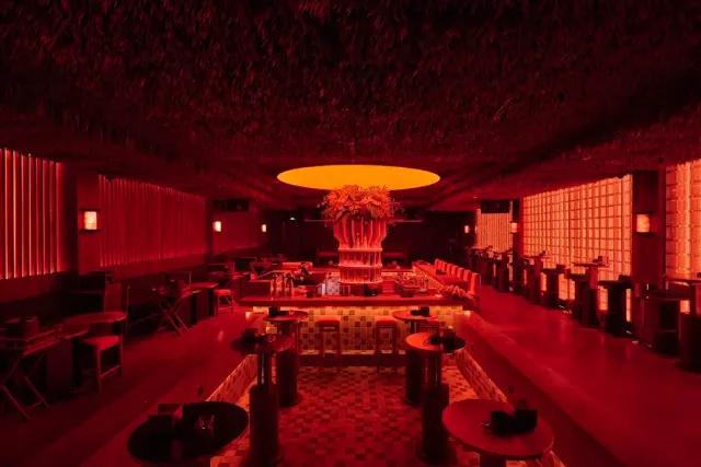 A lounge in red light with a thatched ceiling, a central bar and a large flower arrangement above it