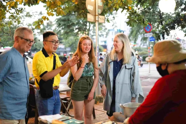 A guide in a yellow shirt explaining to a group of travelers beside a stall in the evening