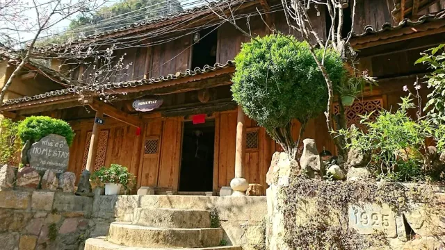 An old wooden house with a tiled roof, stone steps and trimmed shrubs in front