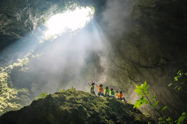 A shaft of light falling into a huge rock chamber, and a group of hikers on a ledge