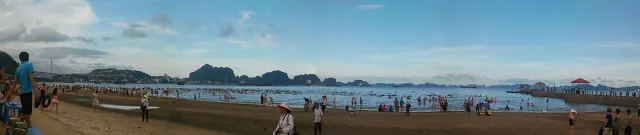 A wide beach with bathers and limestone cliffs on the horizon