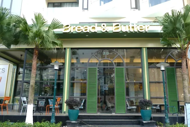 A green and cream facade with gold letters, palms on both sides and green louvered shutters