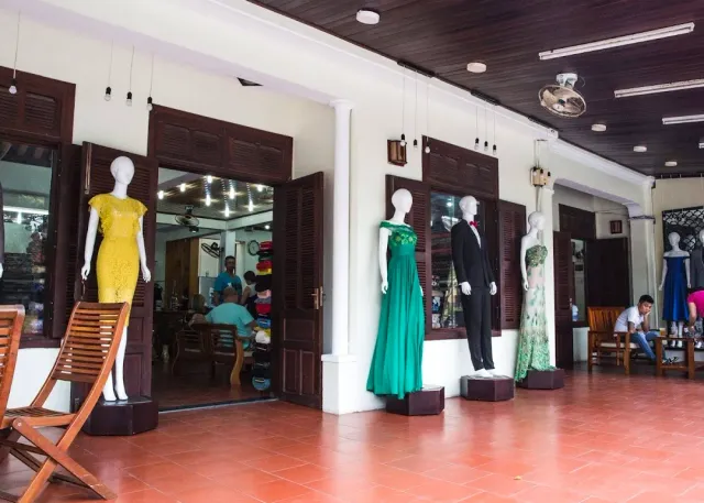A covered porch with mannequins in dresses and a suit, wooden shutters and a terracotta floor