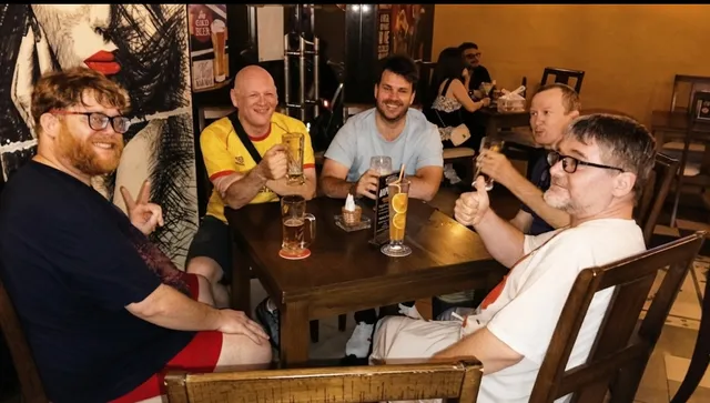 A group of men raising beer glasses around a wooden table in a pub