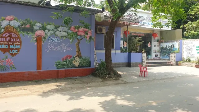 A purple wall with a painted blossoming tree, a red plastic chair and a shaded street beside it