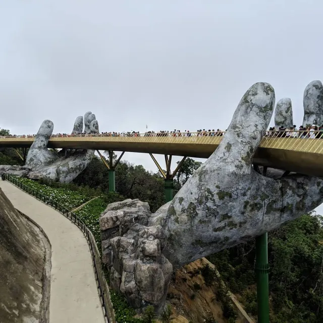 Giant stone hands carrying a golden pedestrian bridge