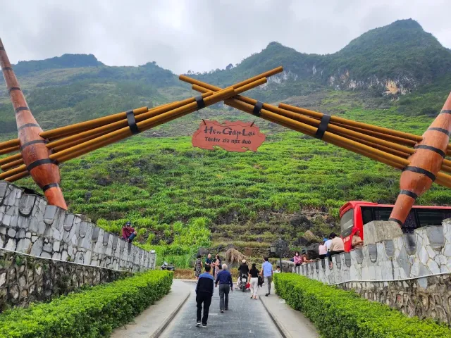 A crossed bamboo gate over a path, with a red wooden sign and green slopes behind