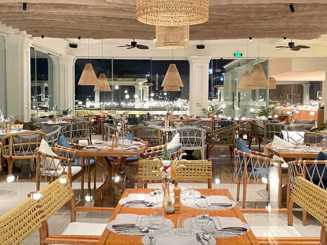 An elegant evening hall with straw lampshades, blue wicker chairs and set tables facing windows
