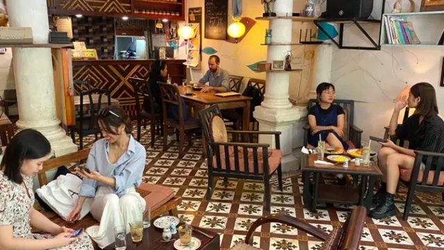 A space with a patterned tile floor, white columns and guests seated in wooden armchairs