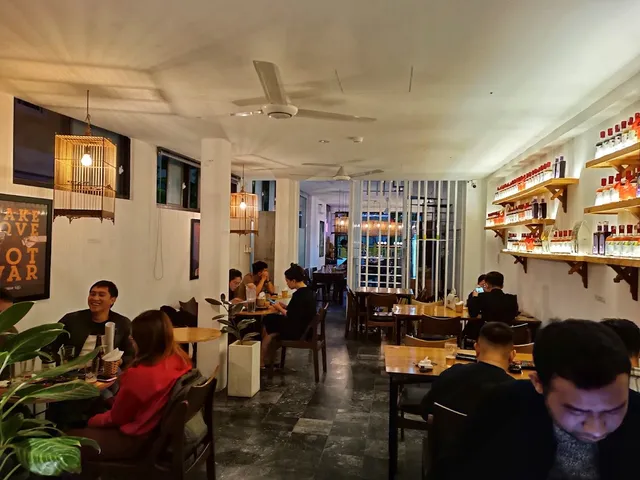 A narrow hall with wooden tables, ceiling fans and shelves of bottles on the wall