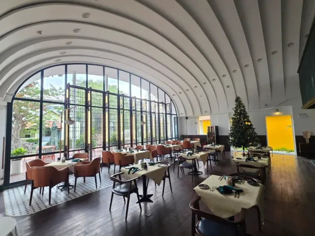 A white vaulted hall with a huge arched window, tables in cream cloths and a fir tree in the corner