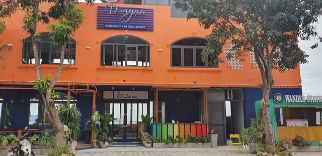 An orange building facade with arched windows, trees and colorful planters at the entrance