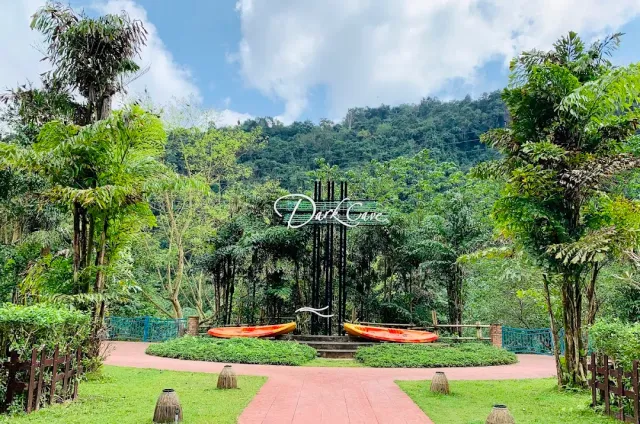 A paved plaza with a decorative sign and orange kayaks, a forested hill behind