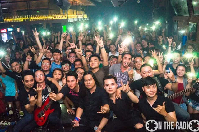 A packed crowd raising hands and phone lights behind a band with guitars at a concert night