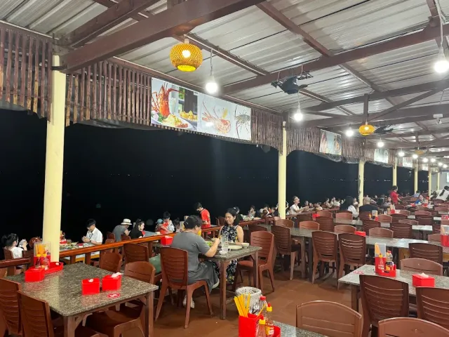 A covered hall in the evening with stone topped tables, brown chairs, diners and seafood posters