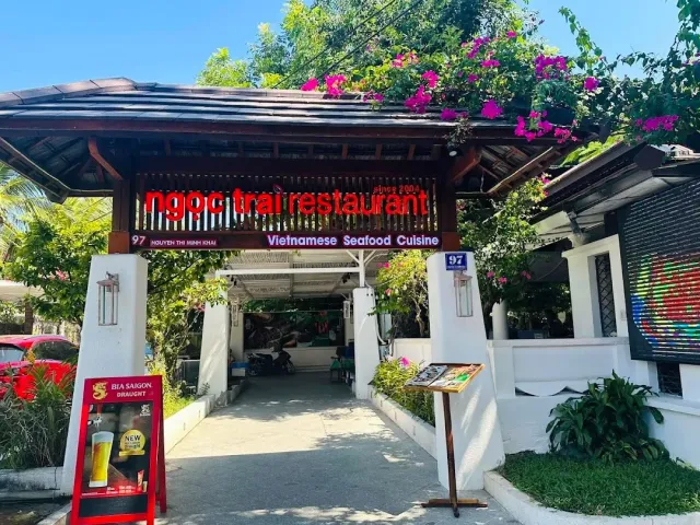 An entrance gate with a tiled roof and a red sign, pink bougainvillea above and a white walkway