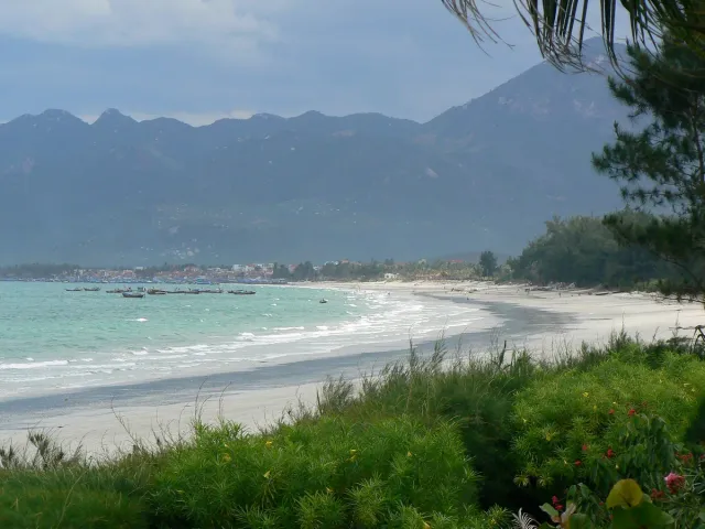 A long white sand bay with shallow water and mountains behind