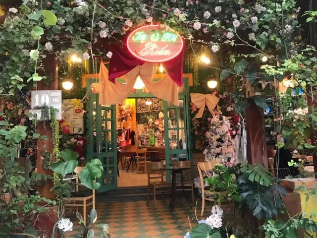 An entrance wrapped in artificial flowers and vines, a neon sign, a red drape and green doors