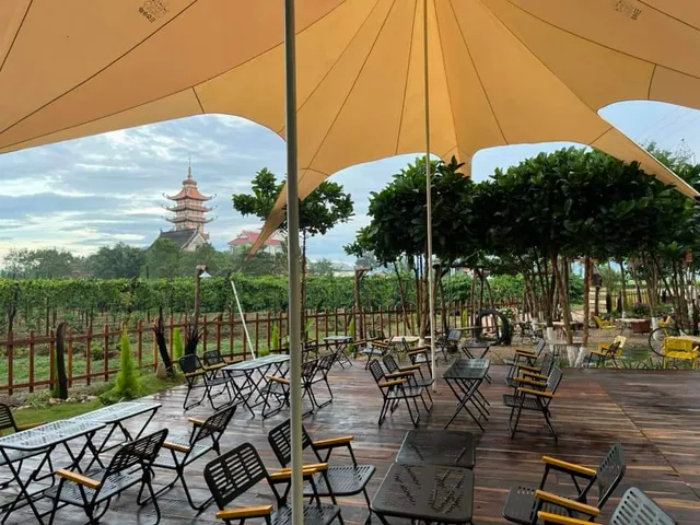 A wooden deck under a fabric canopy with folding chairs, and a tall pagoda beyond the fields