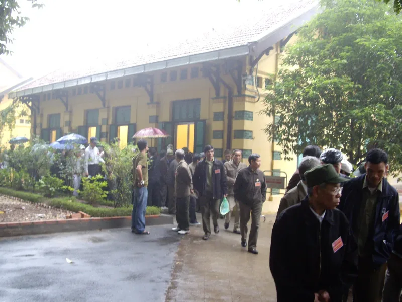 A yellow colonial house with green shutters and a tiled roof in the Presidential Palace compound in Hanoi, with visitors walking along the path in front