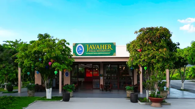 A low building with a green sign between two trees, colorful lanterns and pots at the entrance