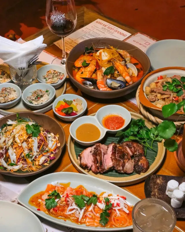 An overhead view of a loaded table, a clay pot with shrimp, salad, sliced meat and sauce bowls