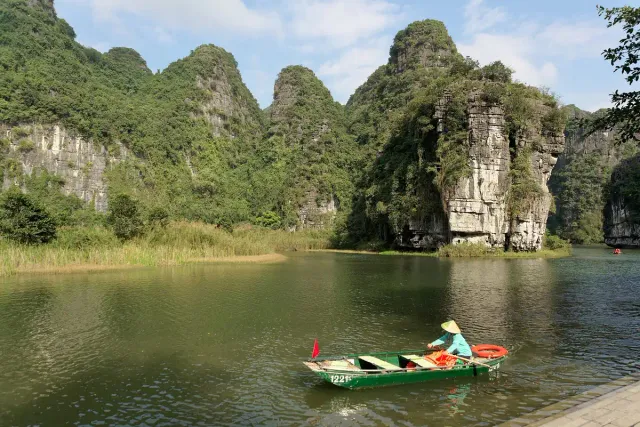 A narrow rowing boat on green water between limestone cliffs