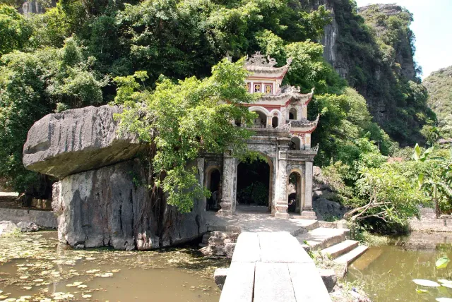 A temple built into a forested cliff face above a pond