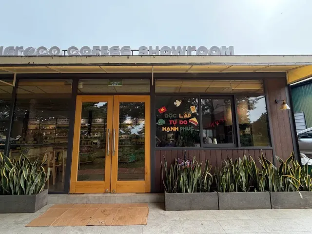 A glass showroom front with light wooden doors and planters holding snake plants