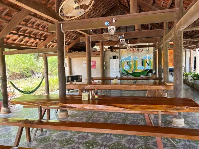 An open wooden pavilion with long wooden tables and benches, a hammock and green scenery outside